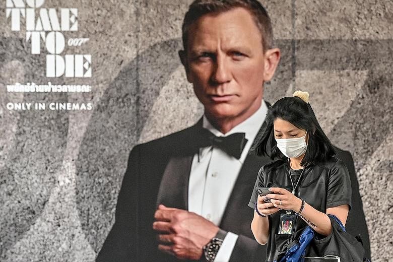 In this photo taken on Feb 28 in Bangkok, a woman walks past a poster for the upcoming James Bond movie No Time To Die, the release of which has been delayed due to the coronavirus pandemic. In A Quiet Place Part II, Emily Blunt (centre) and her fami