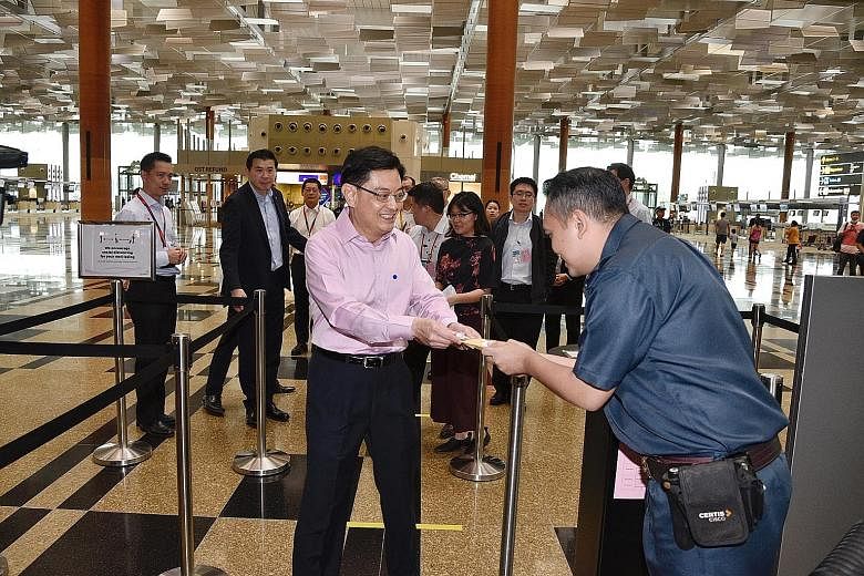 Deputy Prime Minister Heng Swee Keat giving a packet of cookies and an SG United badge from the Civil Aviation Authority of Singapore, packed by Metta alumni youth with special needs, to Certis auxiliary policeman Mohd Nizam at Changi Airport yesterd