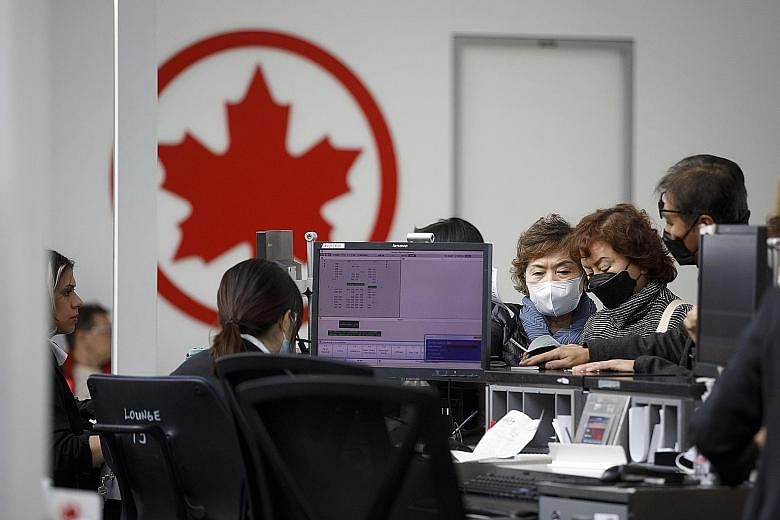 Travellers wearing protective masks checking in at an Air Canada counter in Toronto last month. Air Canada has announced it will cut capacity by up to 90 per cent in the next quarter and temporarily reduce its workforce by about 16,500 to cut costs.