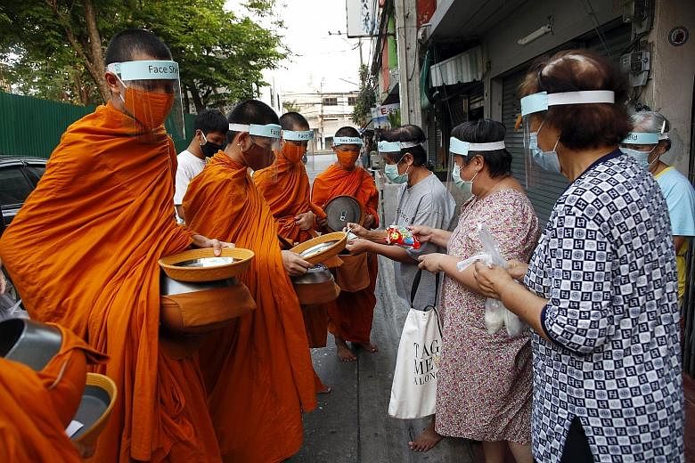 Buddhist monks from Wat Matchantikaram temple wearing masks and face shields receiving alms in Bangkok on Tuesday. The shop closure order announced yesterday is the latest in the series of gradual closures of various venues and restrictions in Bangko
