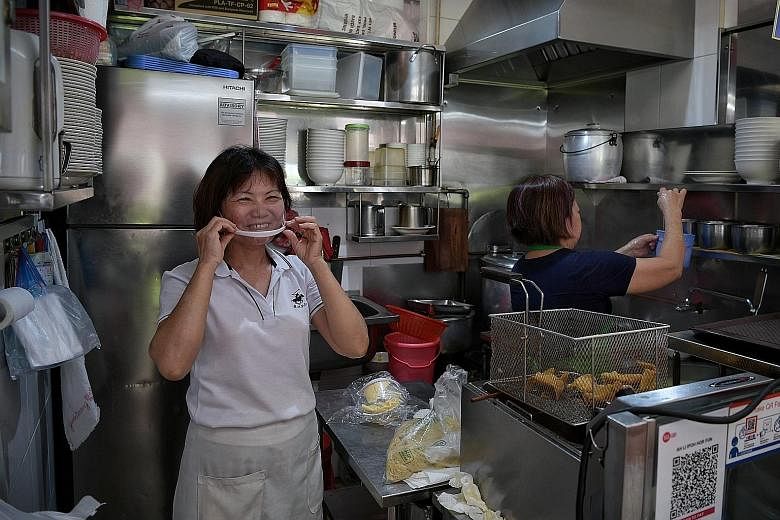 Madam Chen Li, owner of Ah Li Ipoh Hor Fun Fish Dumpling stall at Bedok Food Centre and Market, trying on a spit guard given out by East Coast GRC MP Lee Yi Shyan on Tuesday. More than 3,700 hawker and market stalls have been awarded the SG Clean qua
