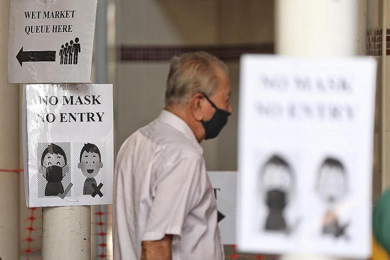 Left: A sign at a wet market in Bedok yesterday reminding patrons to wear masks before entry. Below: A man is made to put on a mask by a security officer before entering Bedok Mall yesterday. Few people were seen outside Lucky Plaza yesterday. The ar