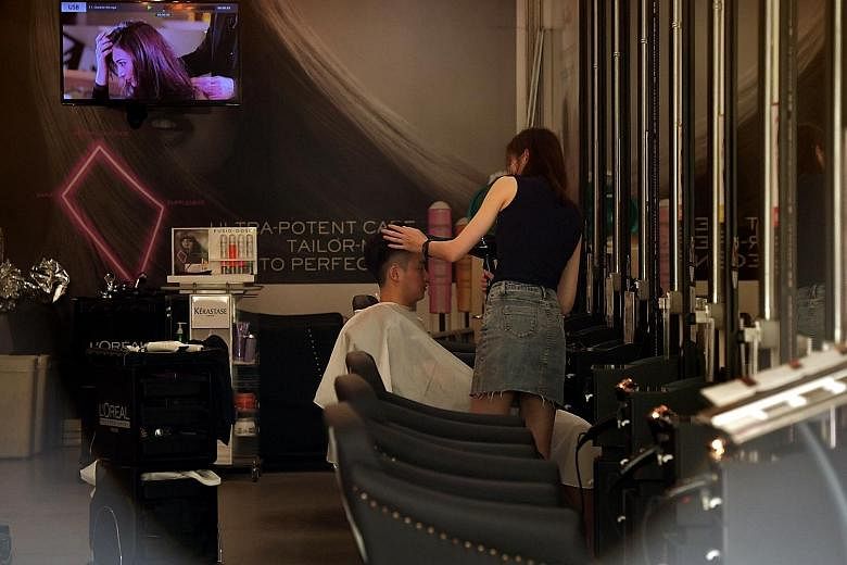 A lone customer at Machi Machi bubble tea shop in Arab Street (above) and a man getting a hair cut at a salon in Toa Payoh (below). Observers said hair salons and food outlets like bubble tea shops may fall into the grey area between what is essentia