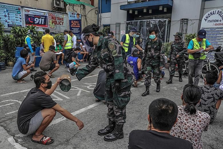 Members of the public, detained for roaming the streets, have their temperatures checked outside a police station in Quezon City, in Manila. PHOTO: AGENCE FRANCE-PRESSE