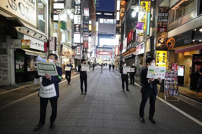 Tokyo metropolitan government employees holding placards calling on passers-by at the Kabukicho entertainment and red-light district on Friday to stay home after the government announced a nationwide state of emergency to prevent the spread of Covid-