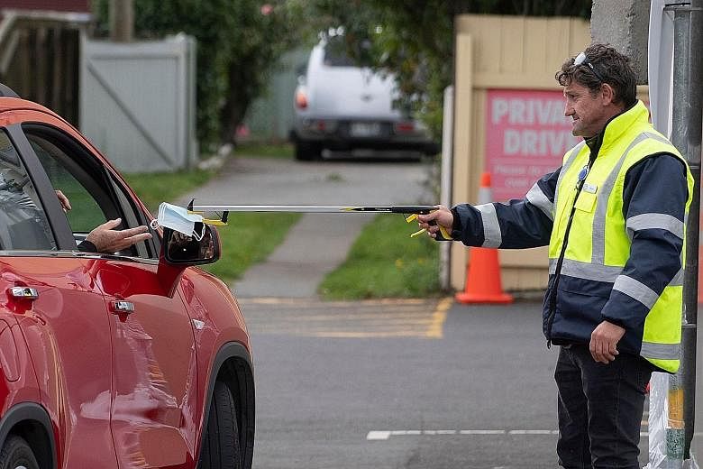 A security guard handing a face mask to a visitor outside a coronavirus clinic near Wellington, New Zealand. The country will start easing a nationwide Covid-19 lockdown next week after claiming success in slowing the spread of the virus, Prime Minis