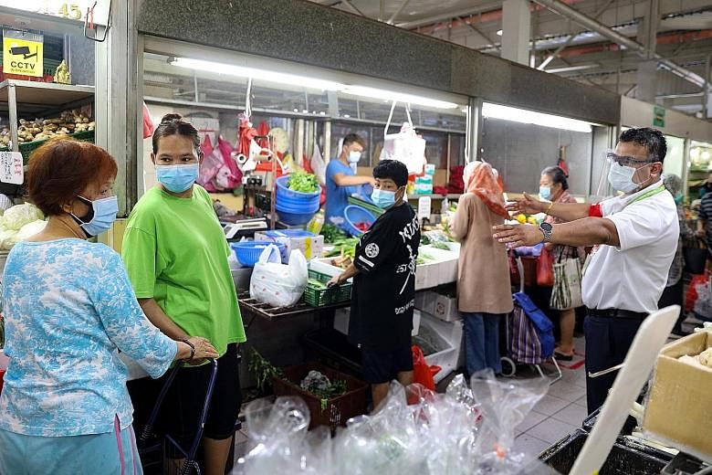 An SG Clean ambassador (right) ensuring shoppers at the wet market at Marsiling Lane adhere to safe distancing rules at around 10.20am yesterday. Despite it being an even date, meaning only shoppers whose NRIC number has an even last digit can enter,