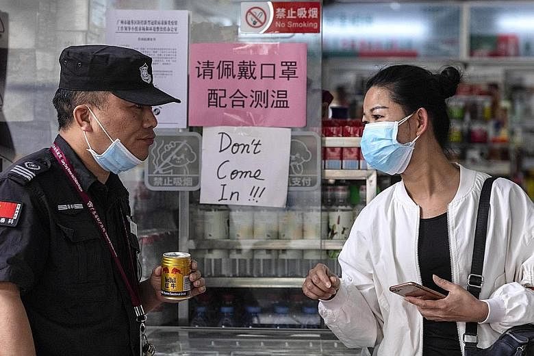 A woman speaking to a guard outside a shop with a sign in Chinese saying people must wear a mask to enter, next to a sign in English that says "Don't come in!!!" in an area popular with the African community in Guangzhou.