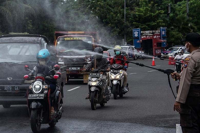 Indonesian policemen spraying disinfectant on motorists at a border checkpoint between Surabaya and its satellite cities to curb the spread of Covid-19 on Tuesday. Indonesia has been in the world spotlight for having the highest fatality rate for Cov