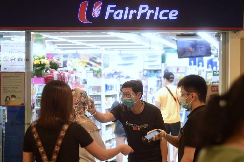 Shoppers having their temperatures checked and NRICs scanned at the FairPrice outlet in Toa Payoh yesterday to facilitate contact tracing.
