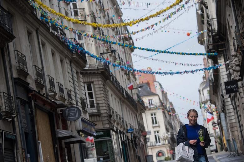 Above: A woman holding Lily of the Valley flowers yesterday in a street decorated with handmade garlands, in Nantes, western France. It is a tradition to gift the flowers to loved ones on May Day in France.