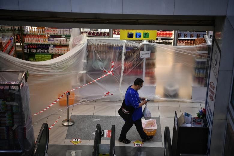 Above: Out-of-bounds sections inside Mustafa Centre have been sealed off with plastic sheets and unused escalators are blocked with red cordon tape. Left: Shoppers and staff at Mustafa Centre yesterday. Only the supermarket section of the mall in Lit