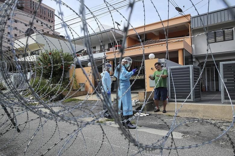 Malaysian health workers checking the details of a resident in an area under lockdown in Petaling Jaya, outside Kuala Lumpur, yesterday. Barbed wire fencing has been installed in the Petaling Jaya Old Town area, closing off three zones to outsiders a