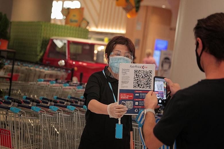 Left: A staff member holding up a QR code for a shopper to complete a contact tracing form before entering FairPrice Xtra at VivoCity last week. Below: A woman getting her temperature taken before entering a McDonald's outlet at White Sands mall yest