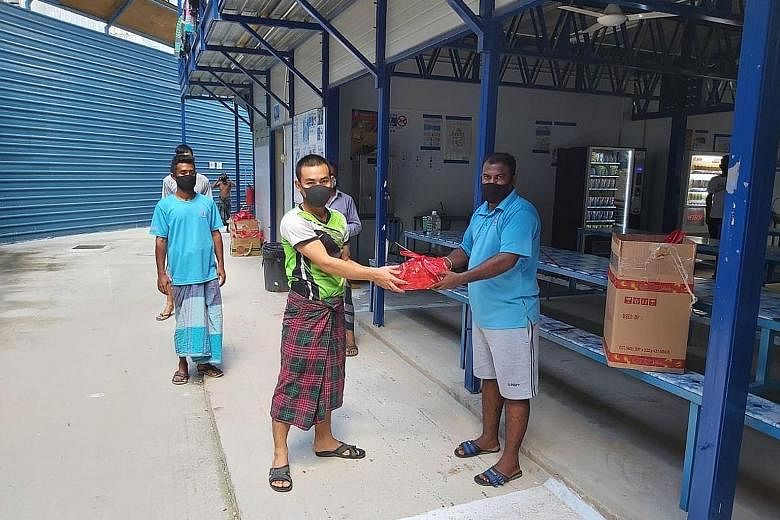 Two migrant workers with a Harvey Norman gift pack containing a portable fan and snacks at their dormitory last Saturday.