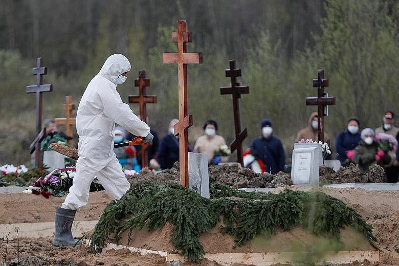 A gravedigger wearing personal protective equipment yesterday in St Petersburg while burying a person who is presumed to have died from Covid-19, with mourners in masks standing at a distance. Russia has almost 250,000 confirmed coronavirus cases, bu