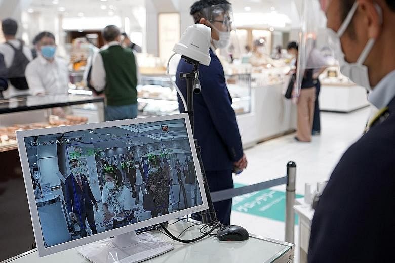 A staff member monitoring a screen that shows people's temperatures during the reopening of a department store's food retailing floor after 11/2 months' closure in Tokyo's Ginza shopping district yesterday. With the number of daily infections on the 