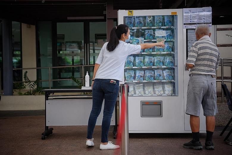 An elderly man collecting his reusable mask from a vending machine at Bishan Community Club yesterday, while some others there chose to collect over the counter instead. Residents queueing for masks at Ang Mo Kio Community Centre yesterday. Over eigh