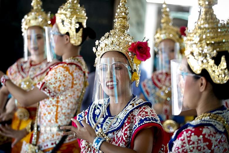 Thai dancers in protective face shields performing on Thursday at Erawan Shrine, a popular tourist site in Bangkok. Starting next Monday, more businesses, such as cinemas, beauty clinics and spas, will be allowed to operate with social distancing rul