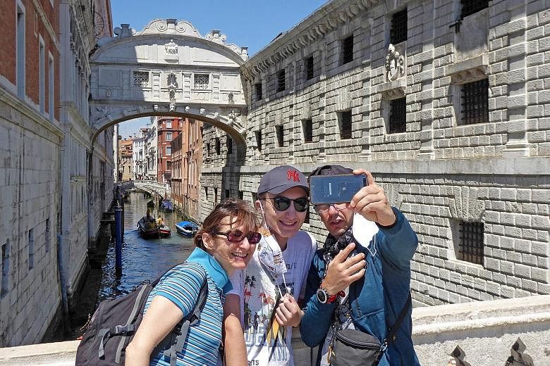 Tourists on San Marco pier in Venice, Italy, with the Ponte dei Sospiri, or Bridge of Sighs, in the background, on Monday. People in the Veneto region are not obliged to wear face masks on the street as the country is gradually easing lockdown curbs 