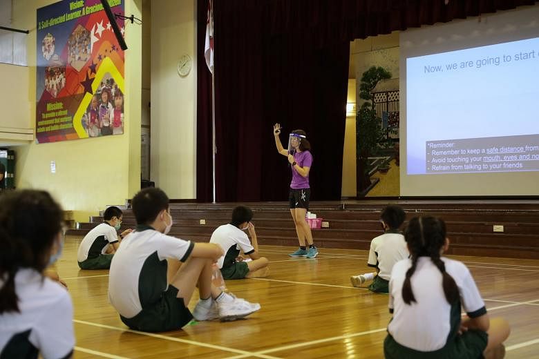 (Left) Xingnan Primary School pupils taking their temperature in the classroom yesterday, the first day of Term 3. (Above) Pupils maintaining safe distancing while being briefed by their physical education teacher Denise Yap in the school hall. They 