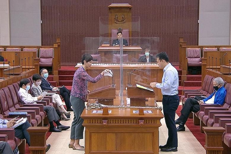 Manpower Minister Josephine Teo wiping down the microphone and podium after answering questions in Parliament yesterday as Minister of State for Manpower Zaqy Mohamad stepped up to speak. Perspex screens were set up in the House as part of safe dista