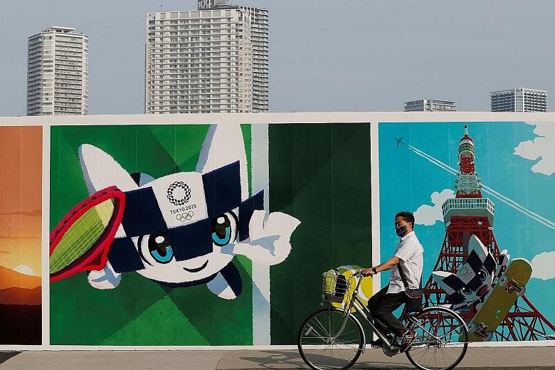 A man in a mask cycling past a poster depicting a mascot of the Tokyo Games, which have been postponed to July 23-Aug 8 next year.