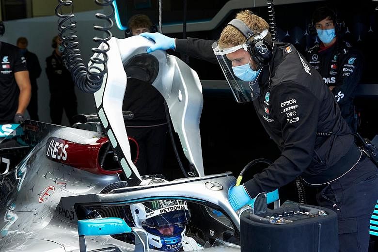 Mercedes driver Valtteri Bottas waiting in the cockpit as his mechanic, wearing a face mask and face shield, prepares the 2018 W09 car at Silverstone circuit yesterday. The Formula 1 team are testing their coronavirus protocols over two days, with Le