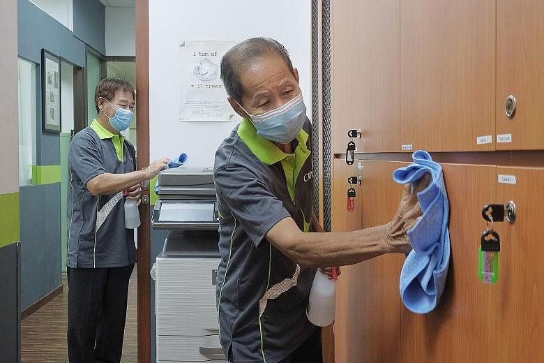 Cleaners Tan Cheng Piew (left), 64, and Pang Tay, 76, at work in an office on Friday. The Covid-19 outbreak has highlighted the plight of essential workers, many of whom continue to go to work often for a low salary, while the rest of Singapore is en