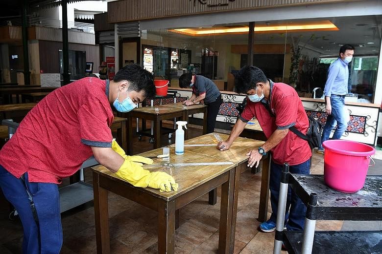 Cleaners removing tape that prevented people from sitting at the tables at Lau Pa Sat yesterday. From Friday, besides dining in at eateries, people can also get together socially in groups of up to five. ST PHOTO: CHONG JUN LIANG