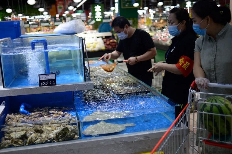 A worker moving produce at the closed Xinfadi market in Beijing. The outbreak last December in Wuhan also started in a market. Above: Chefs waiting to be tested for Covid-19 in Beijing yesterday. Right: Customers buying live seafood at a supermarket 