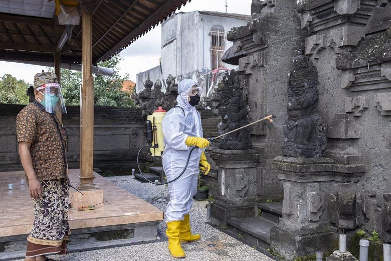 A kite vendor wearing a face mask in Depok, West Java, yesterday. Strict health guidelines are in place for Indonesia's reopenings. A health worker spraying disinfectant at a school in Denpasar, Bali, yesterday. The country is transitioning into a "n