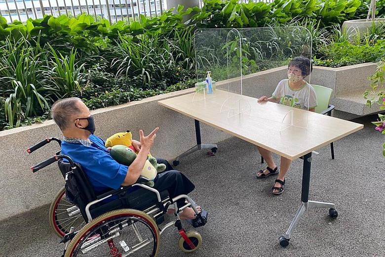 Ms Grace Ang, 39, visiting her father Ang Tiak Huat, 72, at NTUC Health Nursing Home (Geylang East). Clear acrylic partitions separating visitors from residents help to minimise the risk of droplets spreading. PHOTO: NTUC HEALTH