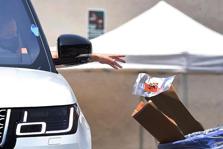 A coronavirus test kit being handed to a driver (left) and another dropped off (right) at a testing site in Los Angeles on Wednesday. California reported more than 7,000 cases overnight, the biggest daily jump so far.