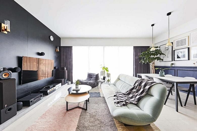 The dark hues from the TV feature wall and audio devices in the living room are contrasted with the light colours found in soft furnishings such as rugs, a fabric sofa and a lounge chair. 