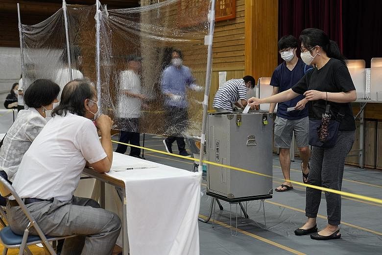 Left: A member of the election management committee disinfecting pencils at a voting station in Tokyo yesterday amid the Covid-19 outbreak. Voter turnout was 55 per cent, down 4.73 percentage points from the last polls in 2016. About 15 per cent cast