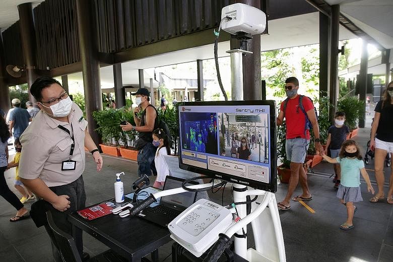 Visitors walking past a thermal scanner and checking in via SafeEntry yesterday before proceeding to the entrance of the Singapore Zoo, where they had their e-tickets scanned. Jurong Bird Park and the River Safari have also reopened, while the Night 