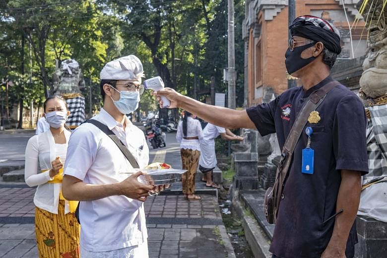 A Balinese security guard taking the temperature of a temple visitor last Friday. Pressure is mounting on the authorities to rescue the battered tourism industry in Bali.