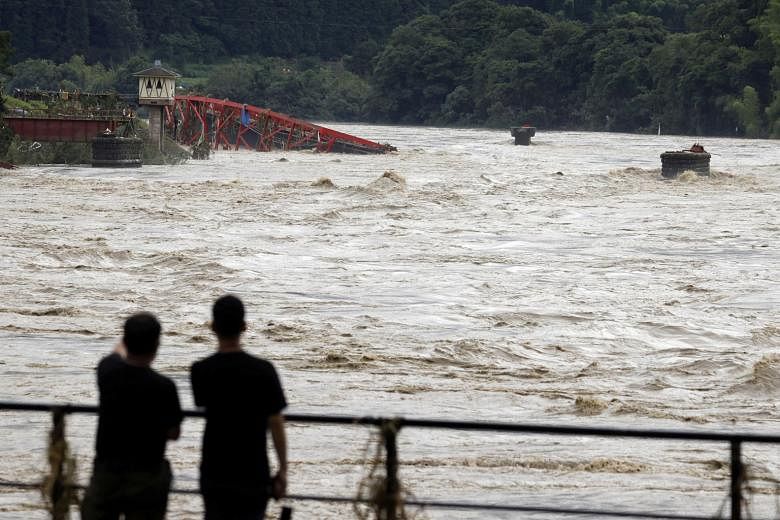 A landslide caused by heavy rain in Ashikita, Kumamoto, yesterday. Evacuation efforts are being hampered by fears over the coronavirus. People watching the swollen Kuma River after torrential rain in Kumamoto prefecture, south-western Japan, yesterda