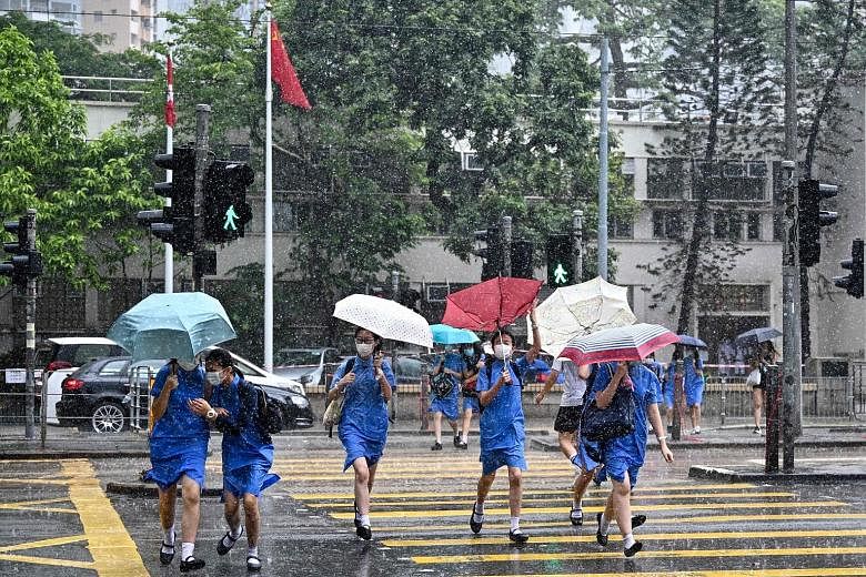 School students crossing a road in Hong Kong during a downpour on Wednesday. Secretary for Education Kevin Yeung said that although some students and parents had recently been infected with the coronavirus, none of the cases were due to the virus bei