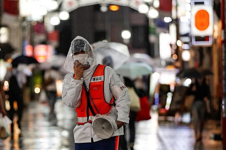A security person in Tokyo reminding people about measures against the coronavirus. Japan is trying to balance containment efforts with economic revival. PHOTO: REUTERS