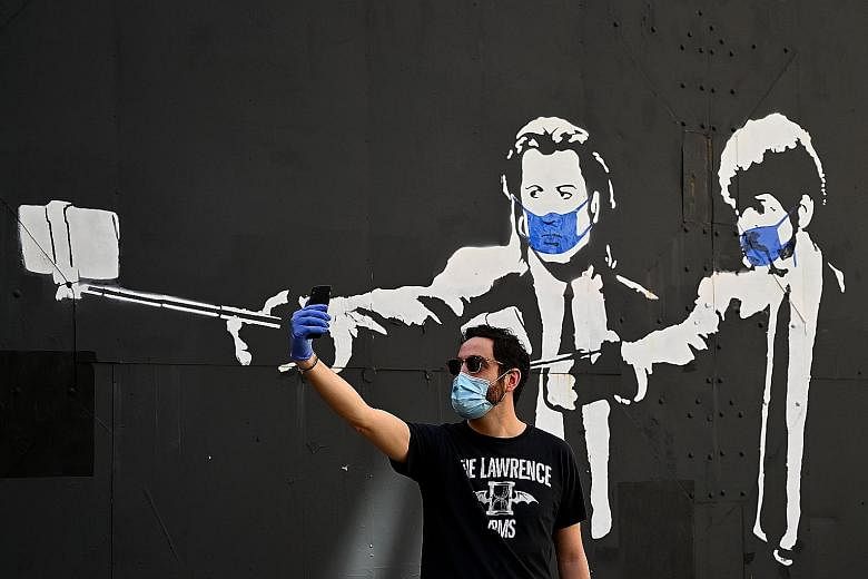 A stencil graffiti of Pulp Fiction actors John Travolta and Samuel L. Jackson wearing face masks in Madrid in May. Workers outside the Diamond Princess cruise ship in Yokohama in February. It became a harbinger of symptomless spreading. Portraits of 