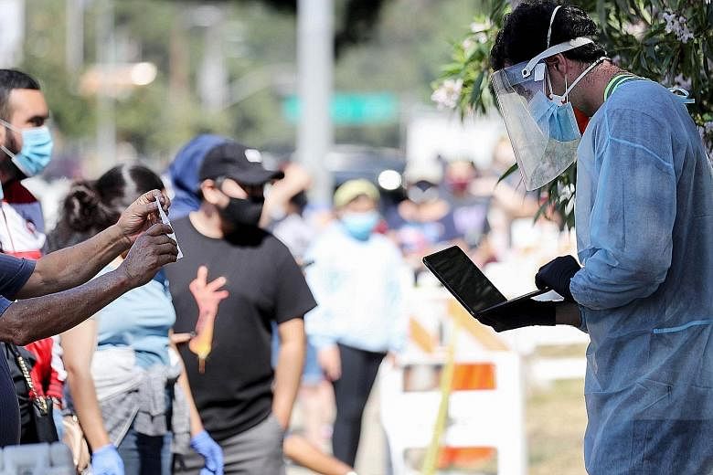 A healthcare worker in personal protective equipment helping people waiting in line to check in at a Covid-19 testing centre at Lincoln Park in Los Angeles last Tuesday.