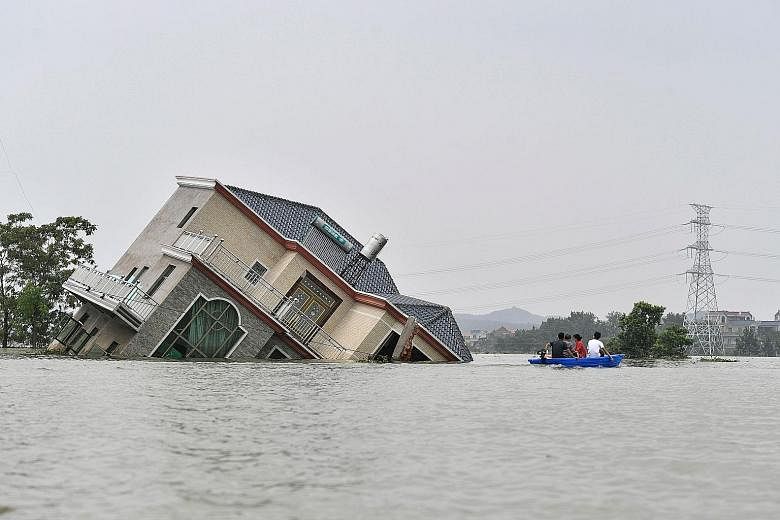 Residents paddling by a damaged house as they flee by boat from the flooded Poyang county in China's central Jiangxi province on Wednesday. PHOTO: AGENCE FRANCE-PRESSE