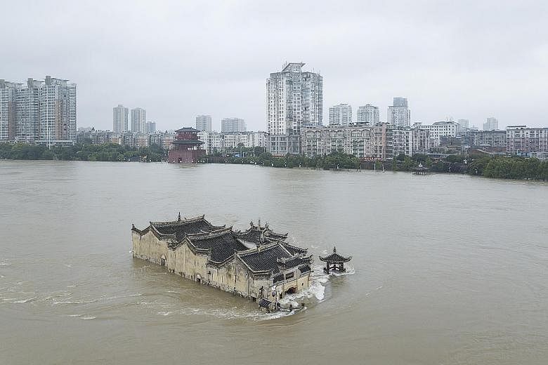 Left: The Guanyin Temple in the middle of the flooded Yangtze River in Ezhou, Hubei province, on Sunday. PHOTO: EPA-EFE Below: People wading through floodwaters with their belongings outside a flooded tourist attraction near the Chao Lake in Hefei, A