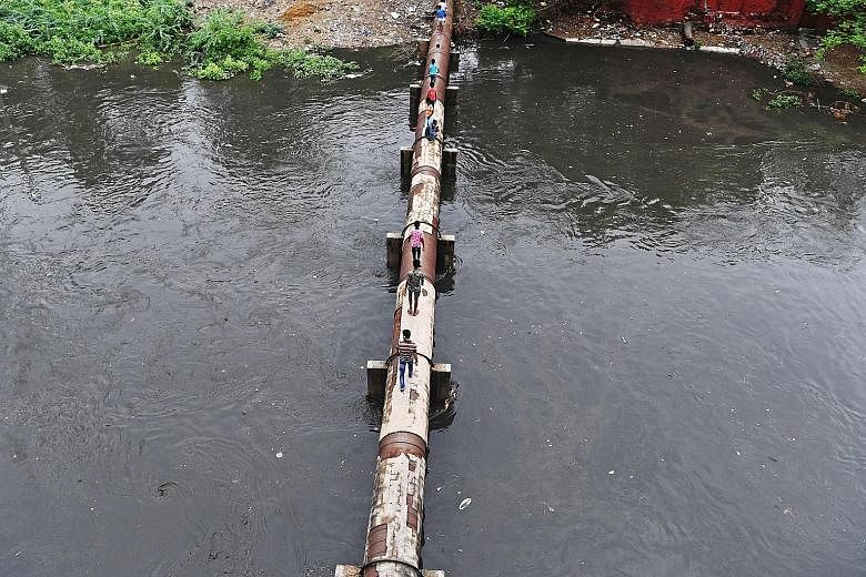 Residents crossing a flooded sewage canal on an elevated water pipeline yesterday after monsoon rainfall in New Delhi. Torrential monsoon rains have swept across India, Bangladesh and Nepal. Hundreds have died in floods and landslides during the curr