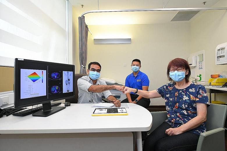 Madam Peggy Tay, whose cancer is in remission after taking the drug combination suggested by AI platform QPOP, fist bumping her oncologist Anand Jeyasekharan, who treated her at the National University Cancer Institute, Singapore. With them is Associ