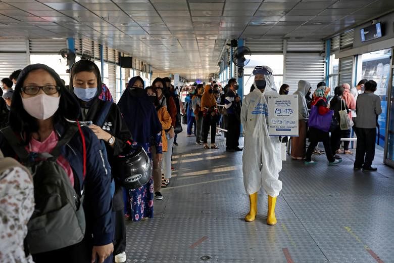 A worker at a central bus hub in Jakarta holding a placard with the total number of positive Covid-19 cases on Monday written on it. Since the middle of the month, some 45 clusters - of two or more simultaneous infections - have emerged as residents 