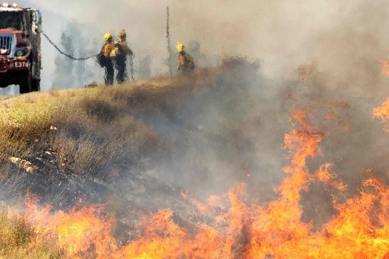 Firefighters, seen through heat from flames, battling the wildfire near Banning, in Southern California, last Saturday. PHOTO: AGENCE FRANCE-PRESSE