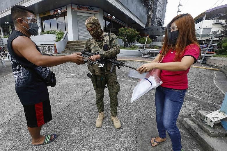 Cyclists riding on the sidewalk as traffic built up at a checkpoint in Marikina city in Metro Manila yesterday, the first day of a stricter lockdown to curb coronavirus infections in the Philippines. PHOTO: REUTERS A Philippine soldier checking the d